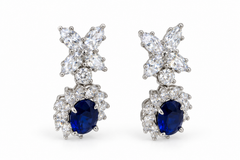 Pair of floral drop earrings with white-stone flower tops and blue oval drops surrounded by white stones on a white background.
